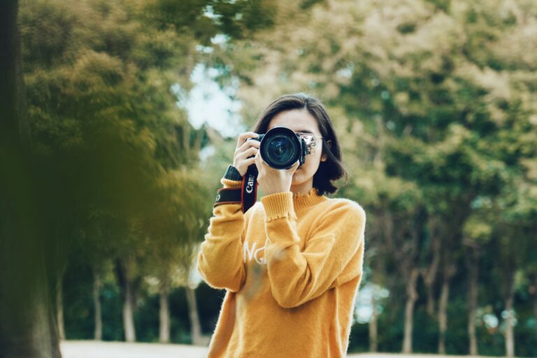Photographe en pull jaune prenant une photo avec un appareil reflex dans un parc arboré